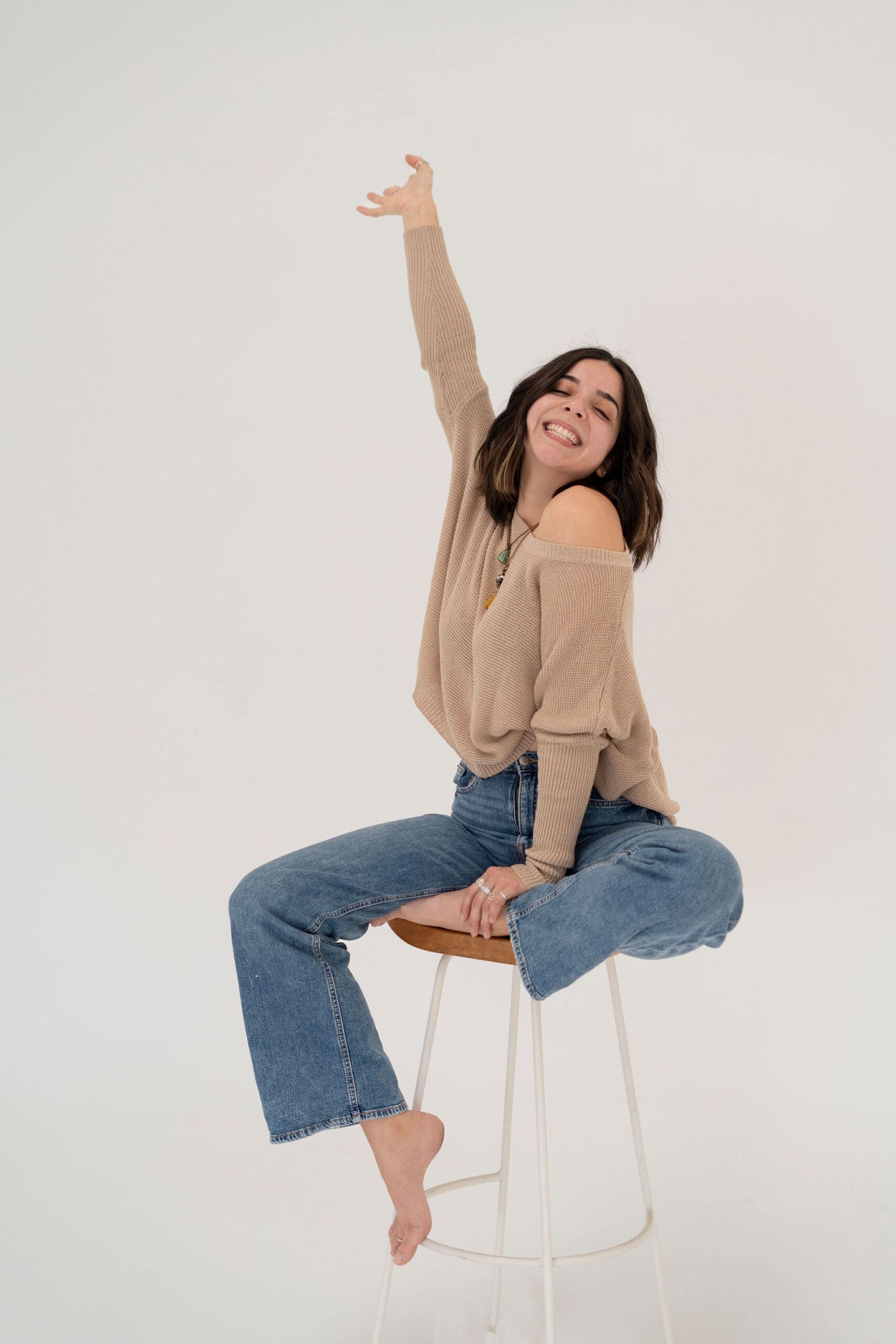 Nicole Sturgeon LLC posing joyfully on a tall stool with her arm lifted, capturing her upbeat brand vibe as a Pinterest manager.